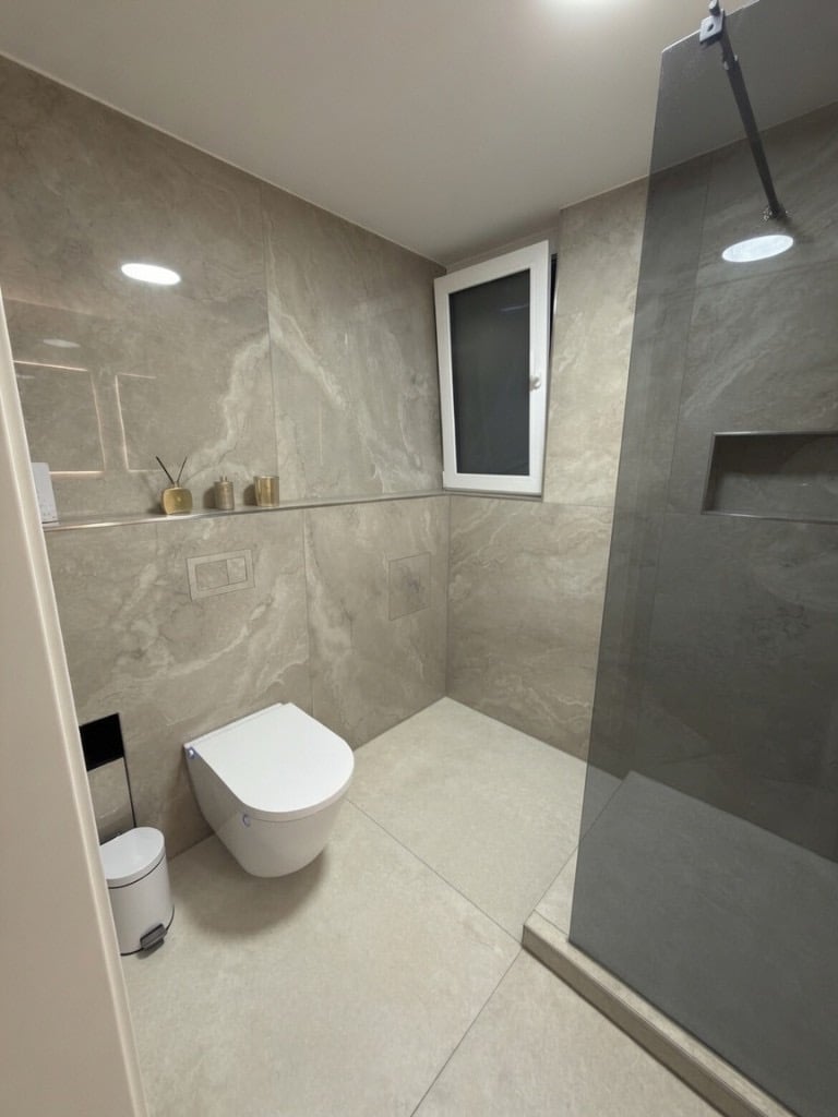 Modernisiertes Badezimmer mit wandhängendem WC und Walk-in-Dusche hinter getönter Glaswand
