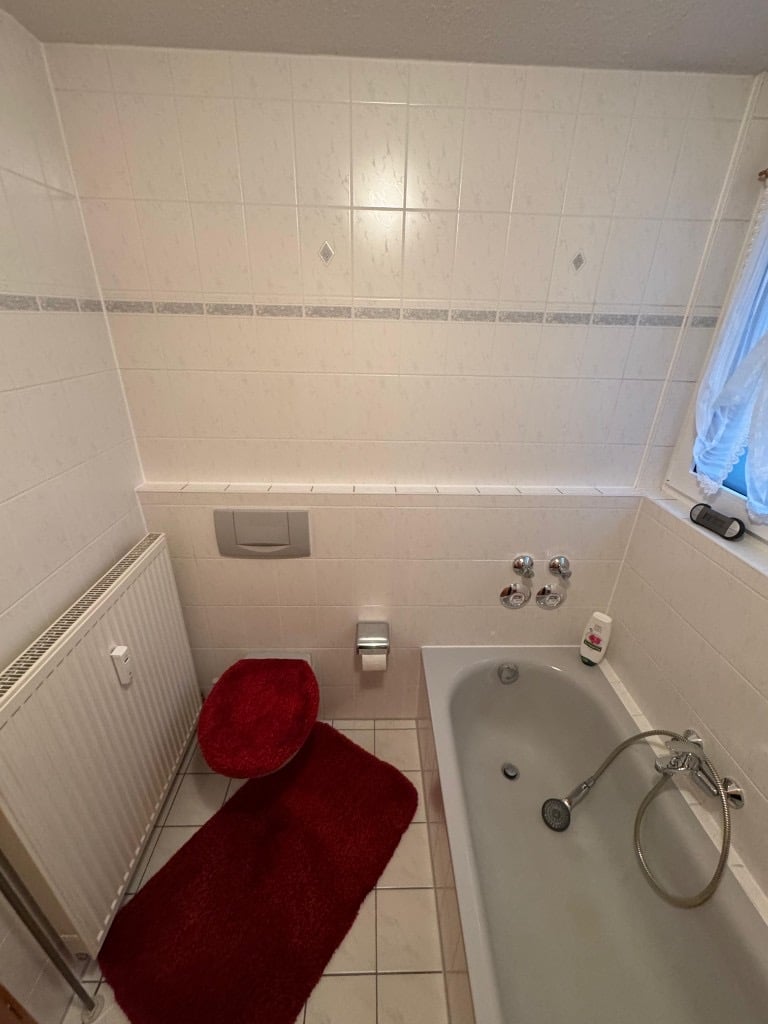 Bestehendes Badezimmer mit Wand-WC, Heizkörper und Badewanne vor der Modernisierung